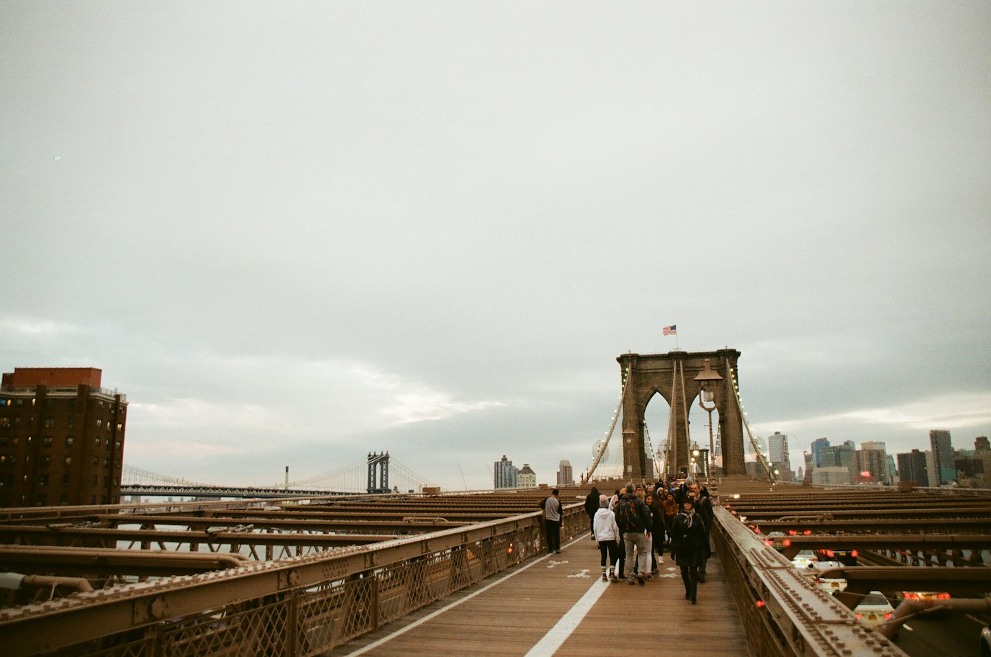 Pedestrians walk along the wooden pathway of the Brooklyn Bridge.